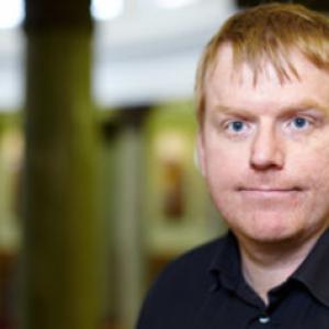 a man faces the camera. He is in a black shirt.